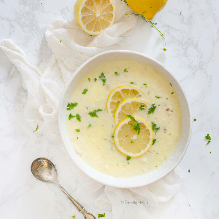 Overhead view of a bowl of chicken lemon rice soup with lemons around it