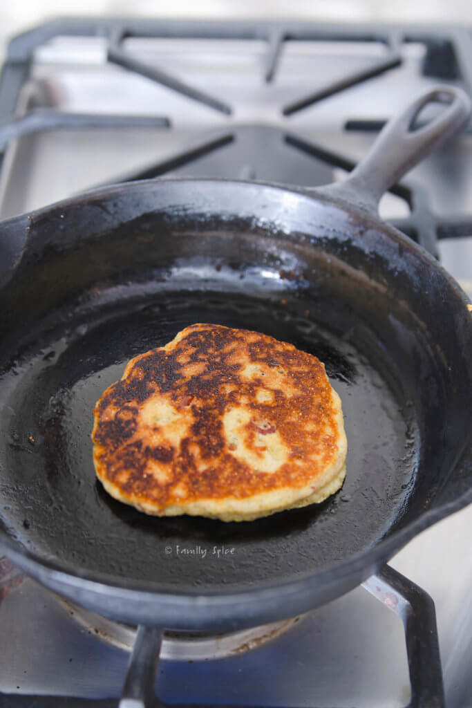 A browned cornbread pancake on a cast iron skillet