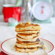 Side view of a stack of cornbread pancakes on a white plate with a scale behind it