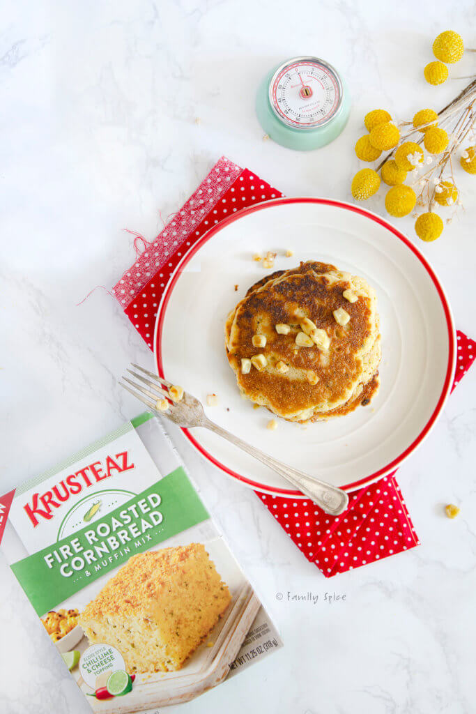 A stack of cornbread pancakes on a white plate with red napkin and box of Krusteaz next to it