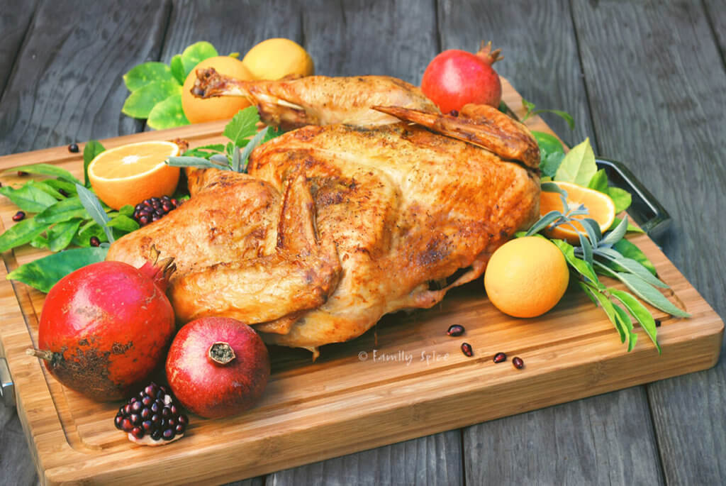 Side view of butterflied turkey with oranges, pomegranates and fresh herbs on a cuttingboard