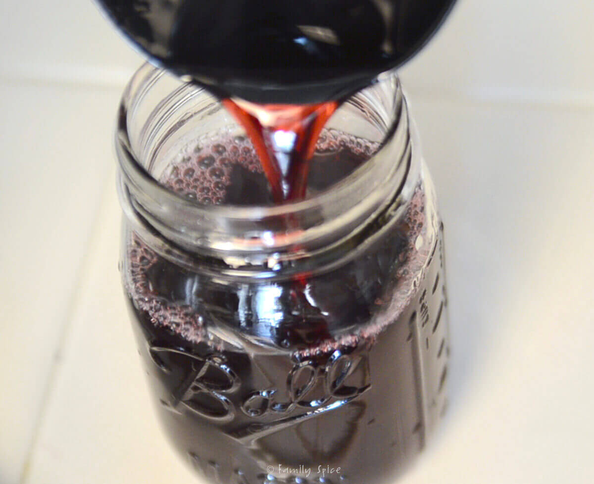 Pouring hot pomegranate jelly mixture into a mason jar