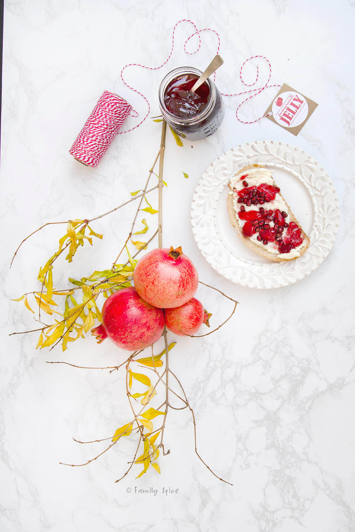 Top view of a tree branch with pomegranates, a plate with toast, cheese and pomegranate jelly