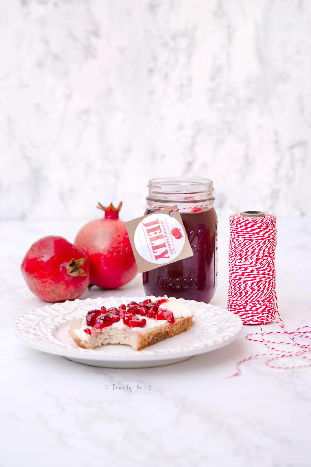 Side view of a plate with toast, cheese and pomegranate jelly and a jar of jelly and pomegranates behind it
