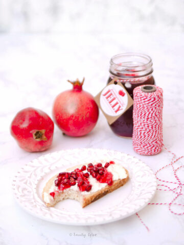 Three quarter view of a plate with toast, cheese and pomegranate jelly and a jar of jelly and pomegranates behind it