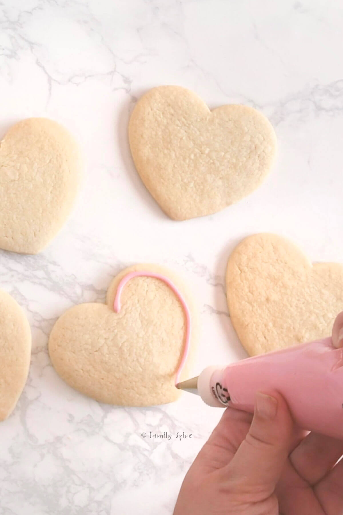 Piping pink royal icing onto a heart sugar cookie