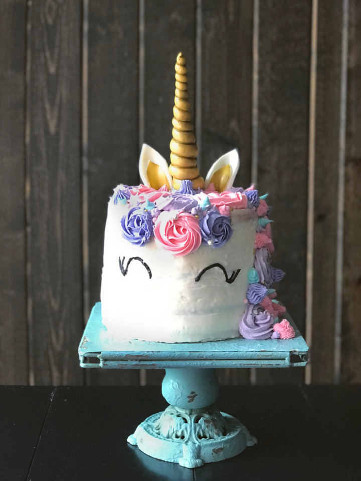 A rainbow unicorn cake frosted in white with pink and purples swirls and golden horn