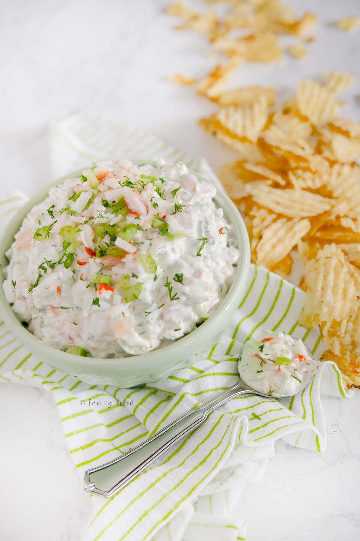 Side view of a bowl with shrimp and crab dip with potato chips around it