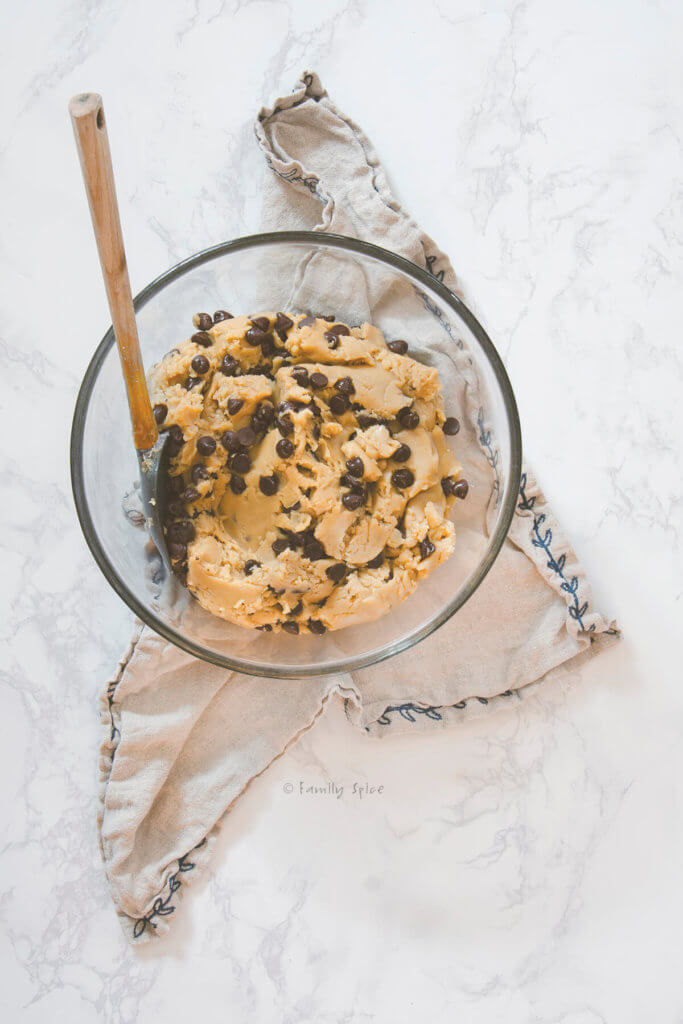 Chocolate chip cookie dough in a glass mixing bowl with rubber scraper