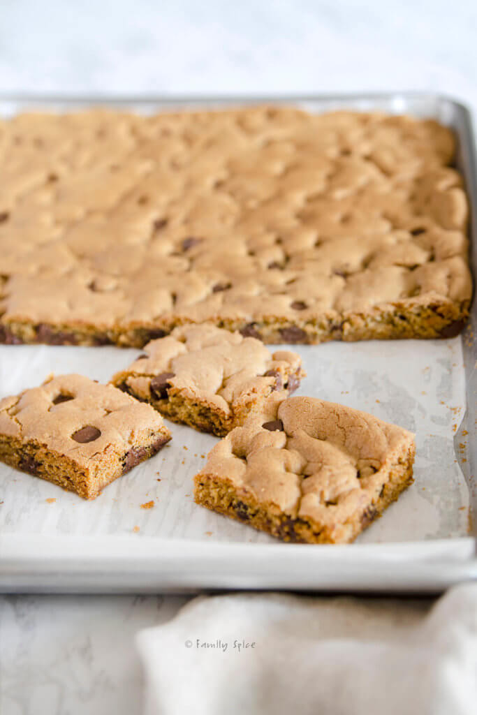 Closeup of 3 chocolate chip cookie bars on a sheet pan with rest of cookie baked behind it