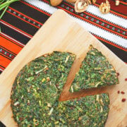 Kuku sabzi on a wood cuttingboard with a slice cut out and herbs and nuts around it