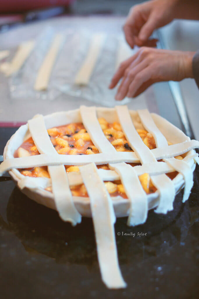 Closeup of assembling the lattice top of an unbaked blueberry peach pie