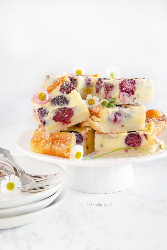 Side view of a stack of blackberry custard bars on a white cake stand on a white background