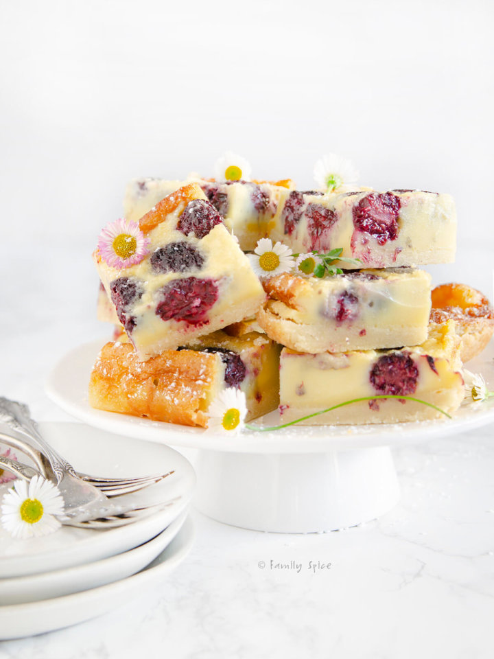 Side view of a stack of blackberry custard bars on a white cake stand on a white background
