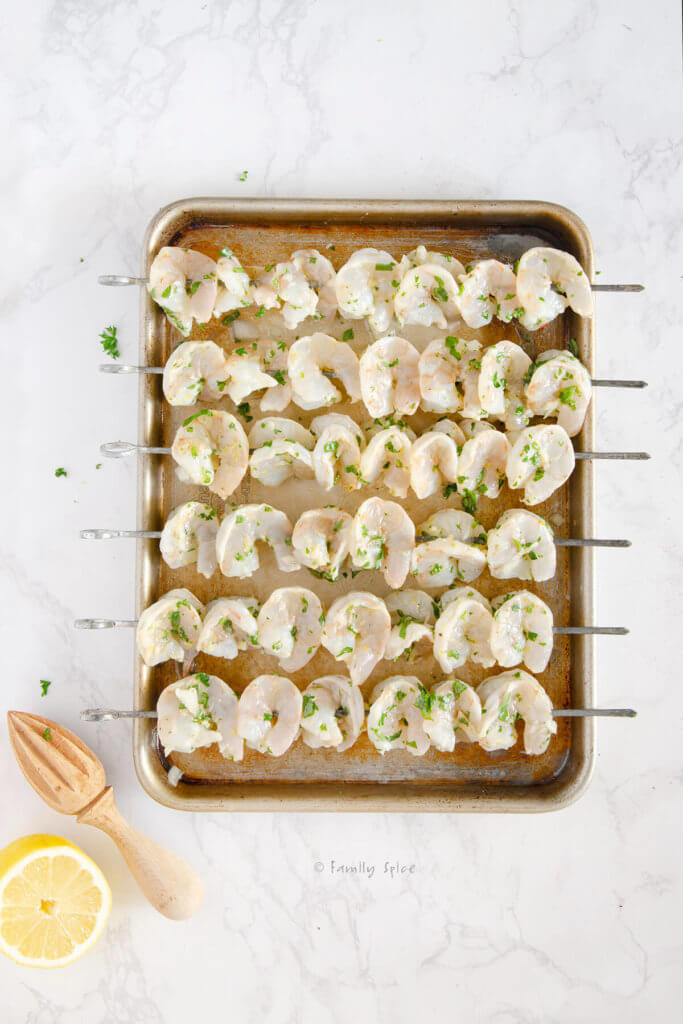 Marinated shrimp on metal skewers placed on a small baking sheet ready to be grilled