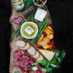Charcuterie board that include Italian meats, feta, Swiss cheese, brie, root vegetable chips, olives, herbs and vegetables