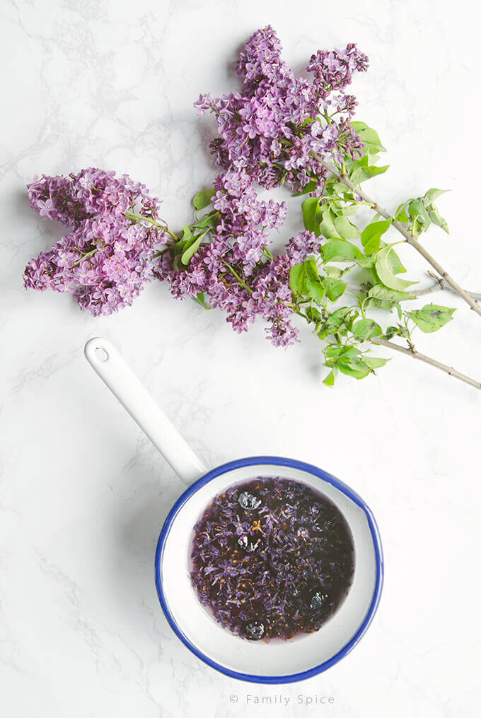 A pot full of lilac blossoms steeping in sugar water to make lilac syrup by FamilySpice.com