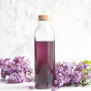 Closeup of a bottle of homemade lilac syrup surrounded by lilacs