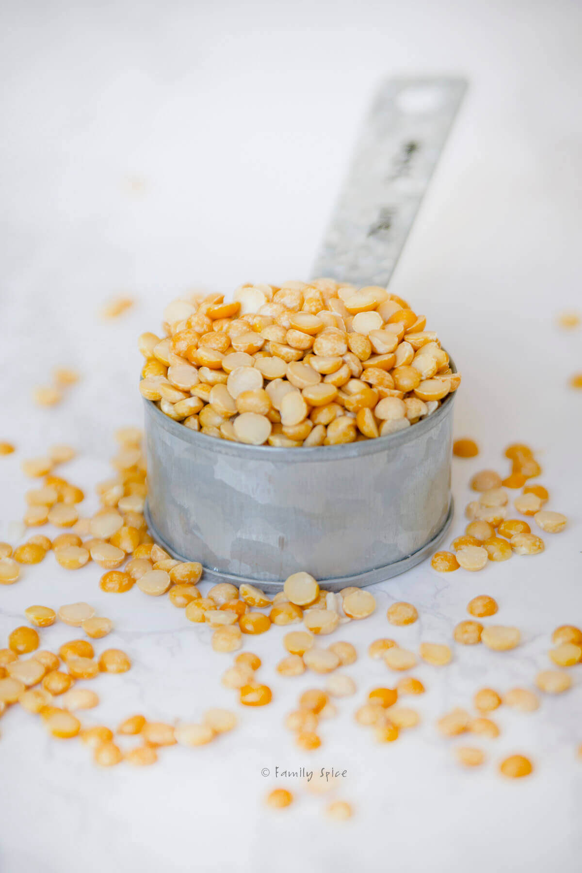 A metal measuring cup with yellow split peas in it