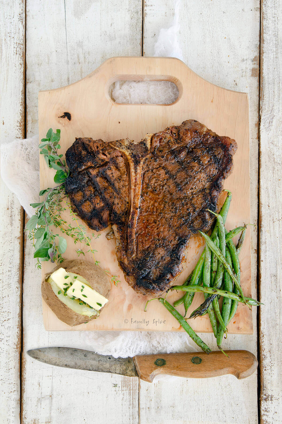 Top view of a grilled porterhouse steak on a cutting board with a potato and green beans