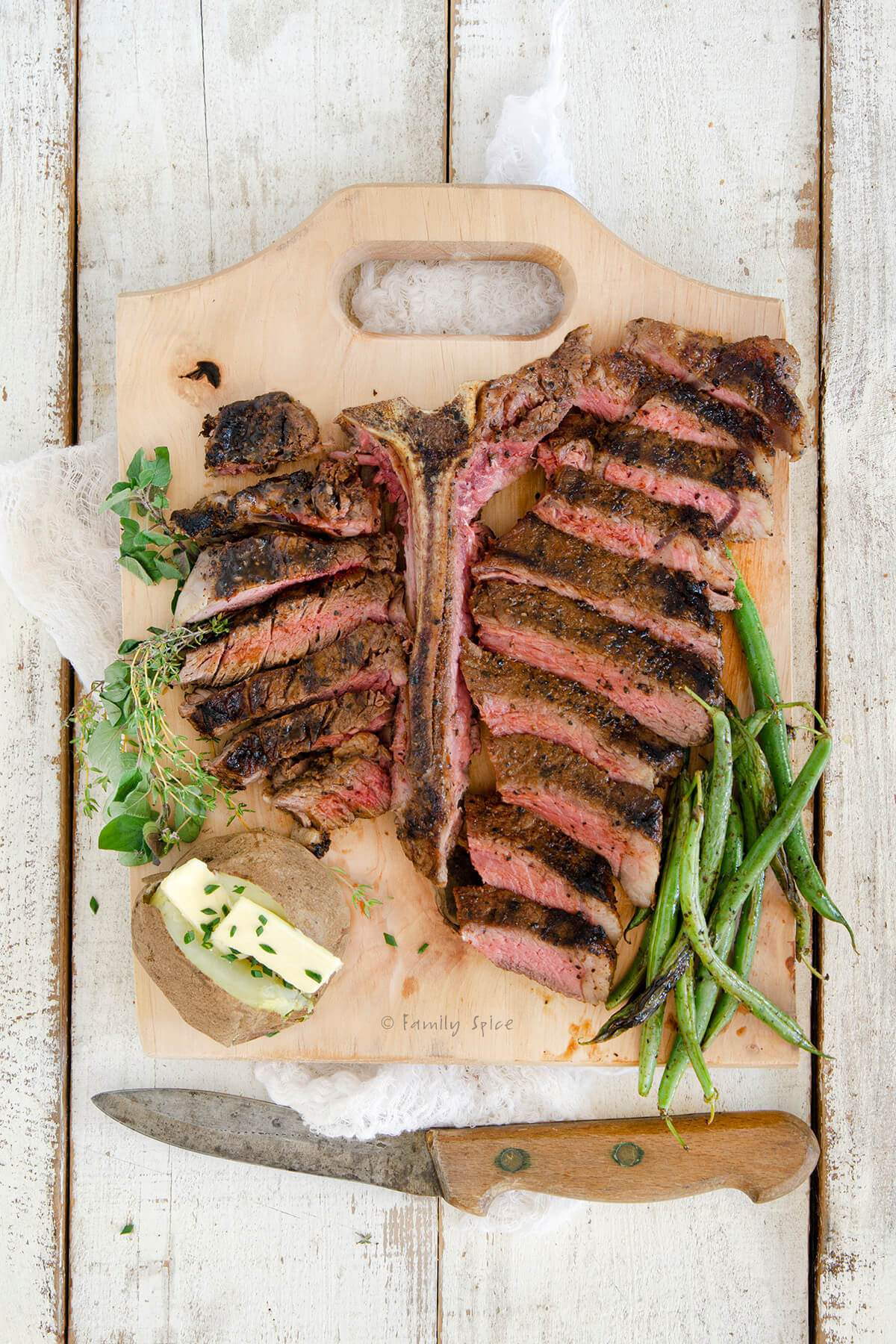 Top view of a sliced grilled porterhouse steak on a cutting board with a potato and green beans