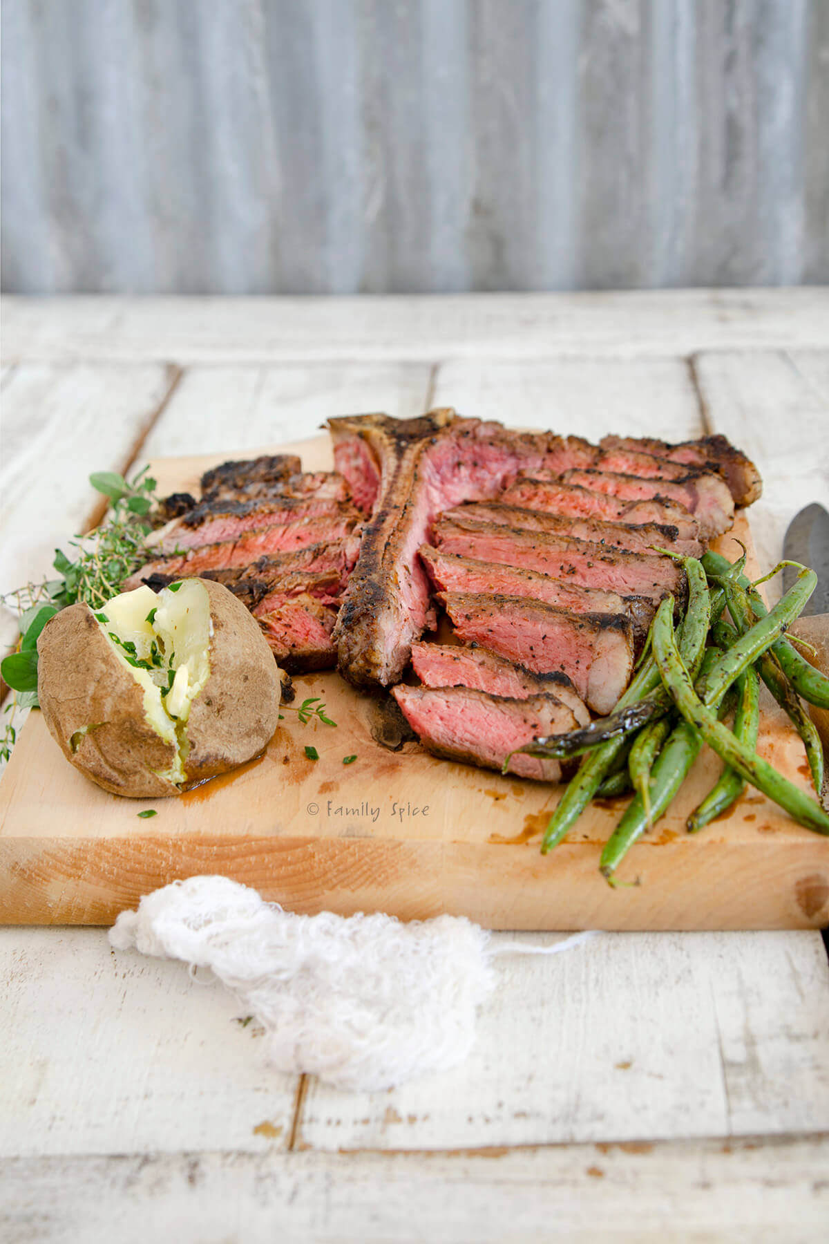 Side view of a sliced grilled porterhouse steak on a cutting board with a potato and green beans
