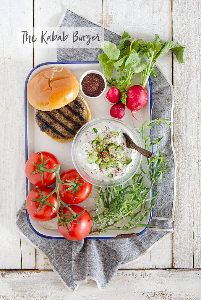 A tray full of vegetables and yogurt to accompany a grilled Persian kabab burger