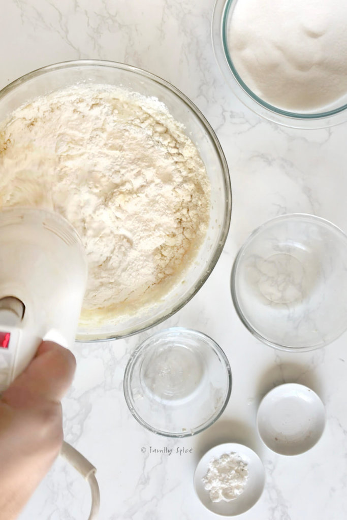 Mixing flour into remaining bakalava cake batter in a mixing bowl with other ingredients in bowls around it