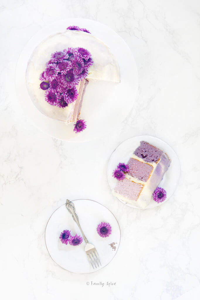 Top view of a purple grape kool aid ombre cake with purple flowers on top and a slice on a white plate next to it