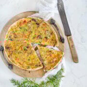 Top view of a pulled pork quiche on a wood tray with fresh herbs and a knife next to it