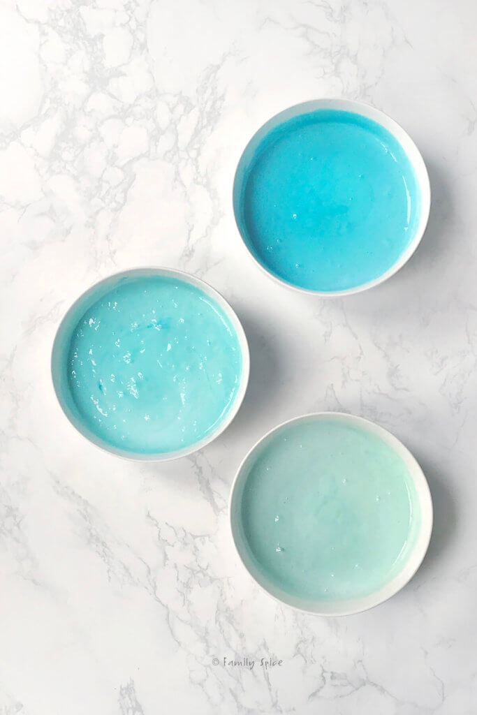 3 bowls of cake batter with various shades of blue raspberry