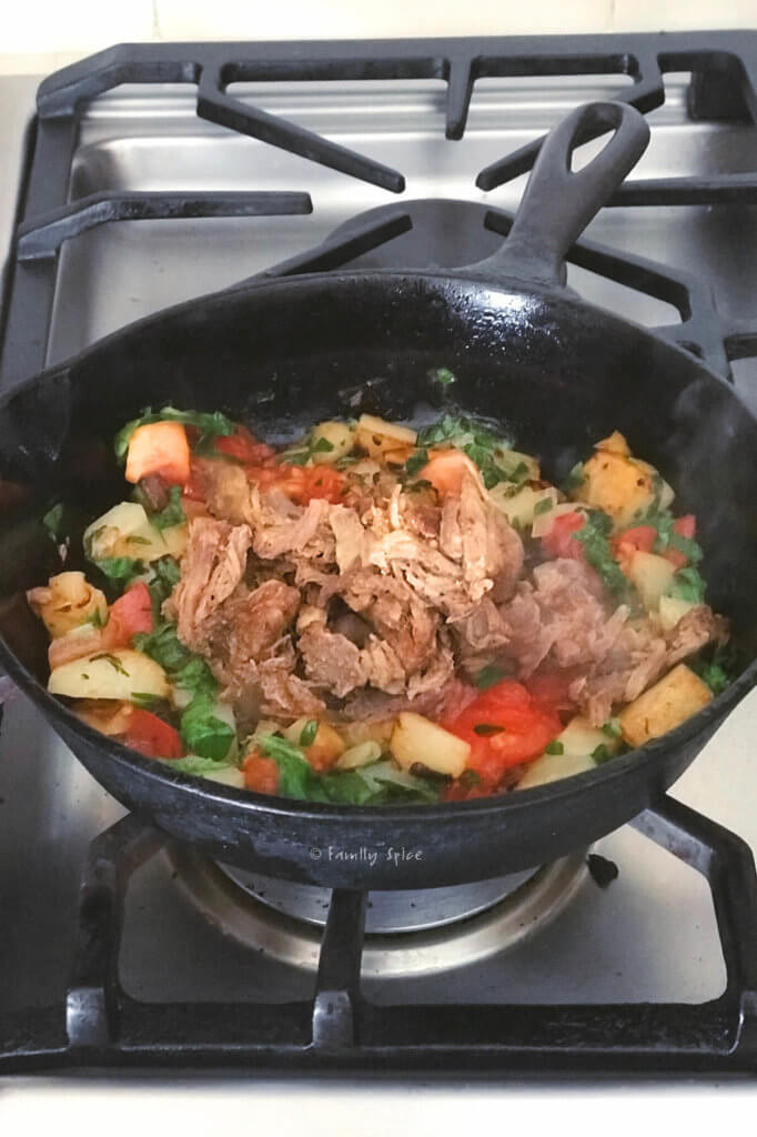 Pulled pork added to potato tomato mixture in a cast iron pan