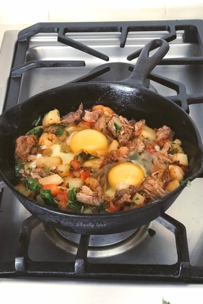 Two eggs added to pulled pork hash in a cast iron pan