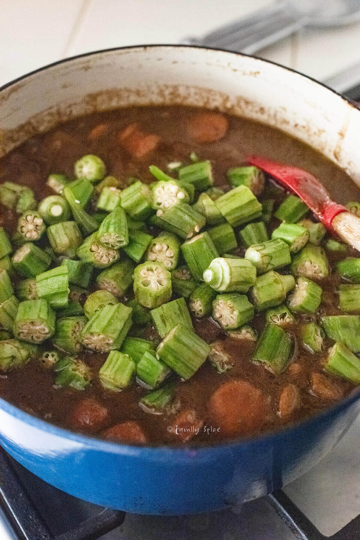 Adding chopped okra to the rest of chicken and sausage gumbo in a pot