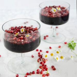 Side view of two dessert glasses with pomegranate gelatin, topped with pomegranate arils.