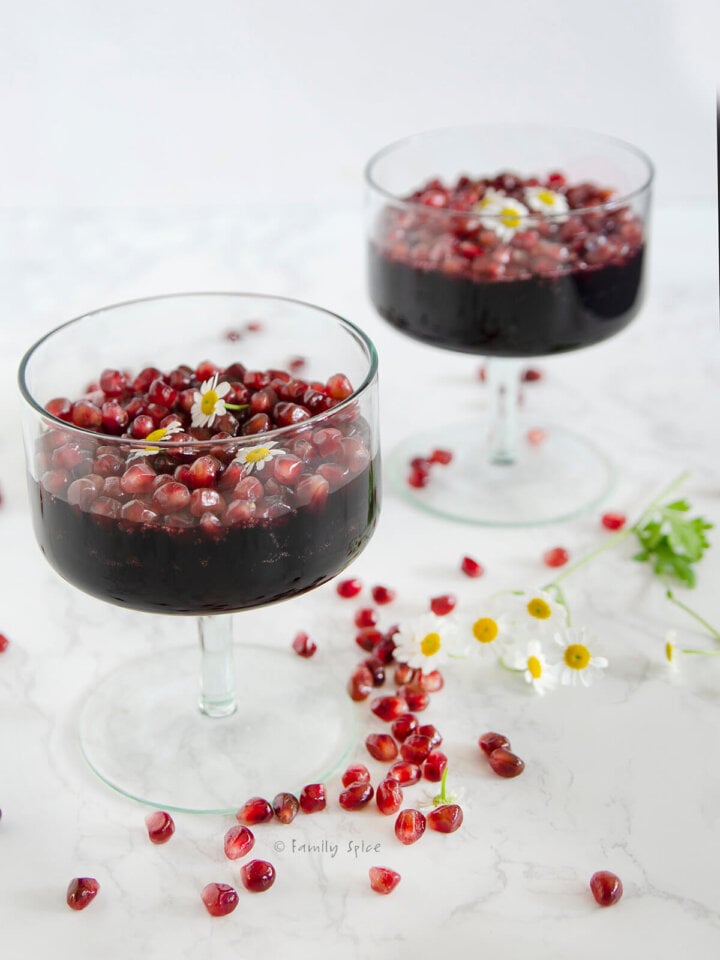 Side view of two dessert glasses with pomegranate gelatin, topped with pomegranate arils.