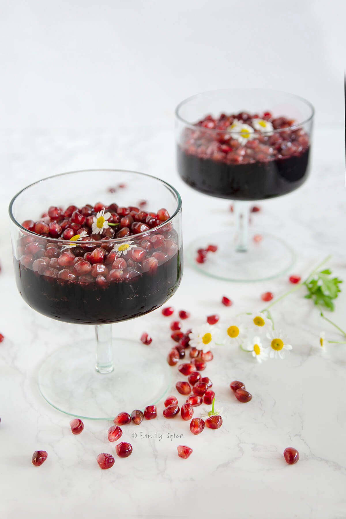 Side view of two dessert glasses with pomegranate gelatin, topped with pomegranate arils.