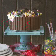 Ice cream cake surrounded by Kit Kats and topped with candies and cookies on a cake stand