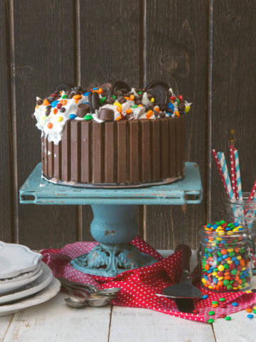 Ice cream cake surrounded by Kit Kats and topped with candies and cookies on a cake stand