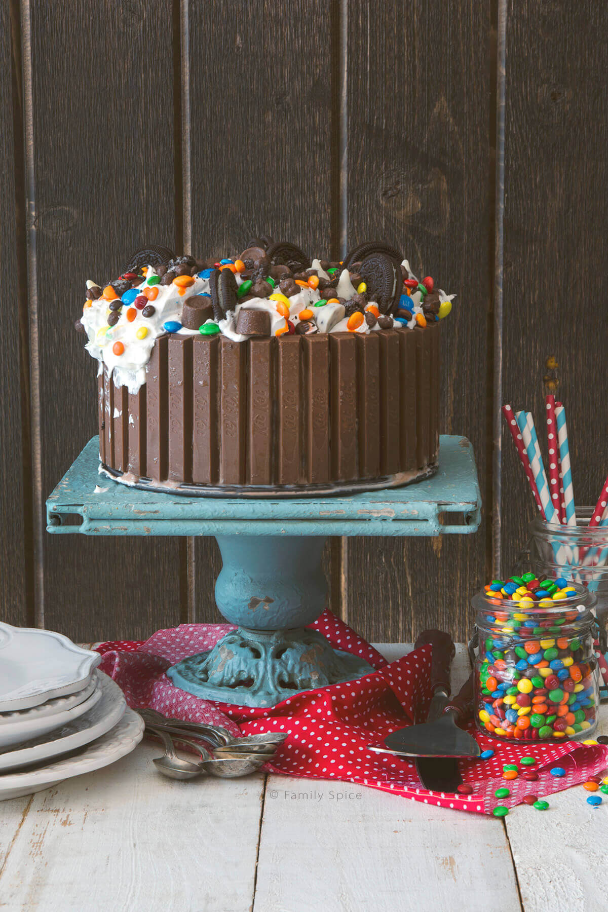 Ice cream cake surrounded by Kit Kats and topped with candies and cookies on a cake stand