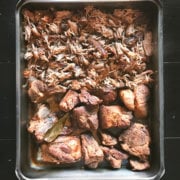 Overhead view of a roasting pan half filled with roasted pork shoulder and half filled with shredded pulled pork
