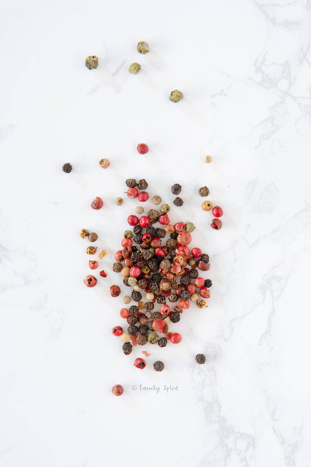 Assorted peppercorns on a white marble background