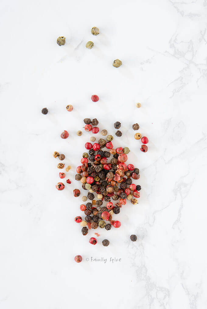 Red, black, white and green peppercorns on a white background by FamilySpice.com