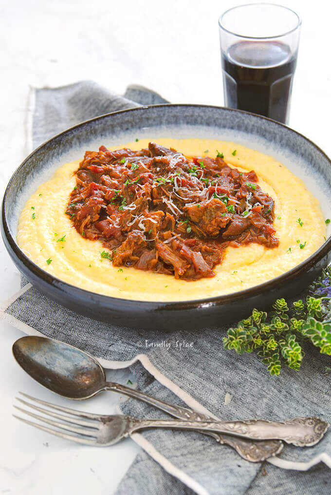 Closeup shot of a shallow bowl of polenta topped with pulled pork ragu by FamilySpice.com