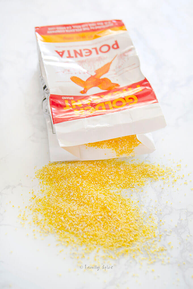 A bag of polenta cornmeal spilled on a white marble countertop by FamilySpice.com