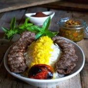A plate full of basmati rice with saffron and koobideh kabob with roast tomatoe, sumac, herbs and torshi