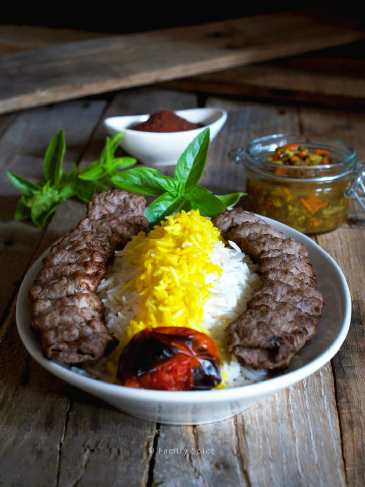 A plate full of basmati rice with saffron and koobideh kabob with roast tomatoe, sumac, herbs and torshi