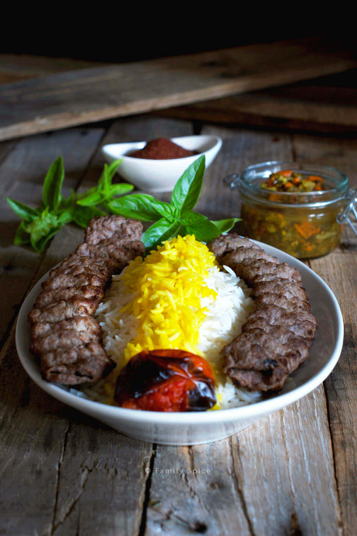 A plate full of basmati rice with saffron and koobideh kabob with roast tomatoe, sumac, herbs and torshi