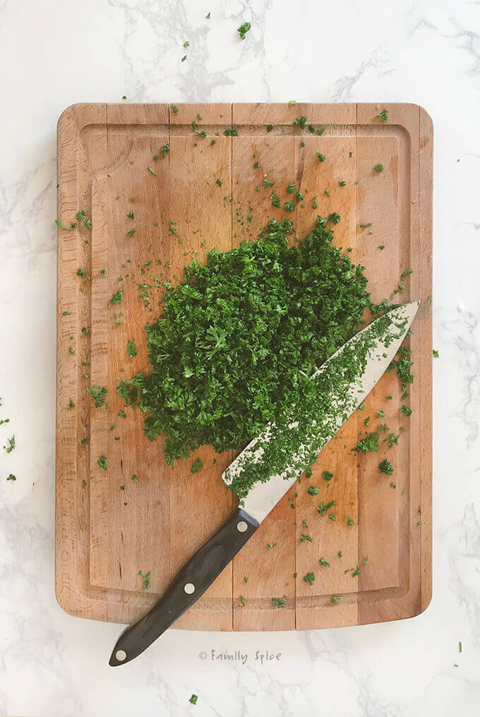 Overhead shot of chopped parsley onions on a wooden cutting board with a knife by FamilySpice.com