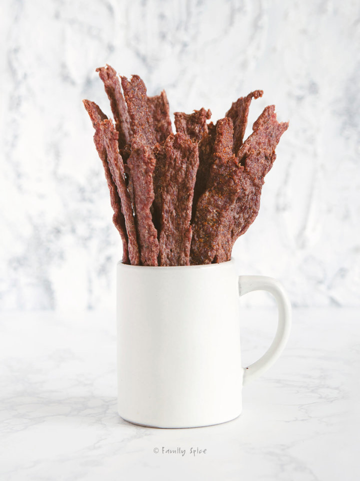 Side view of a white mug with sticks of ground beef jerky in it